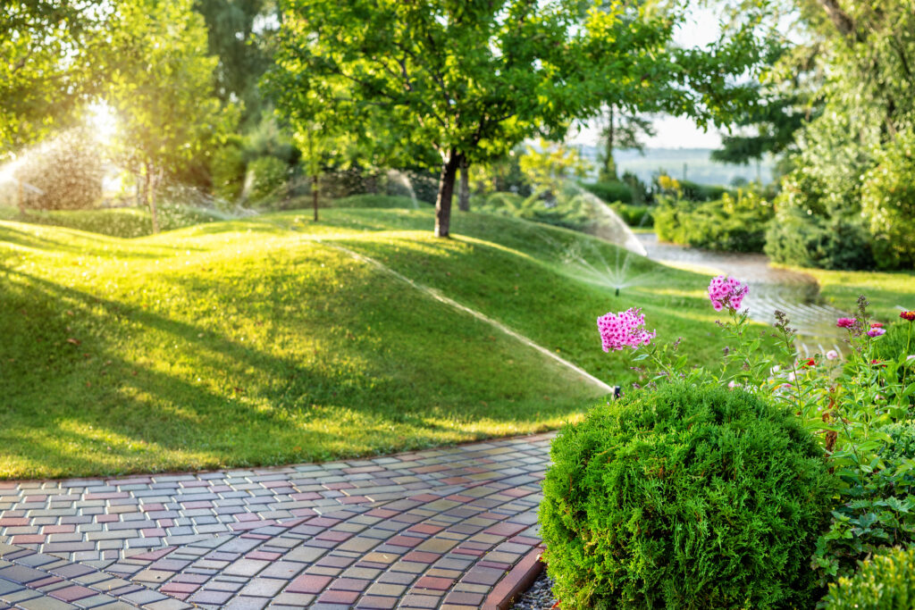 Sprinklers and irrigation system watering grass, flowers, bushes near brick path